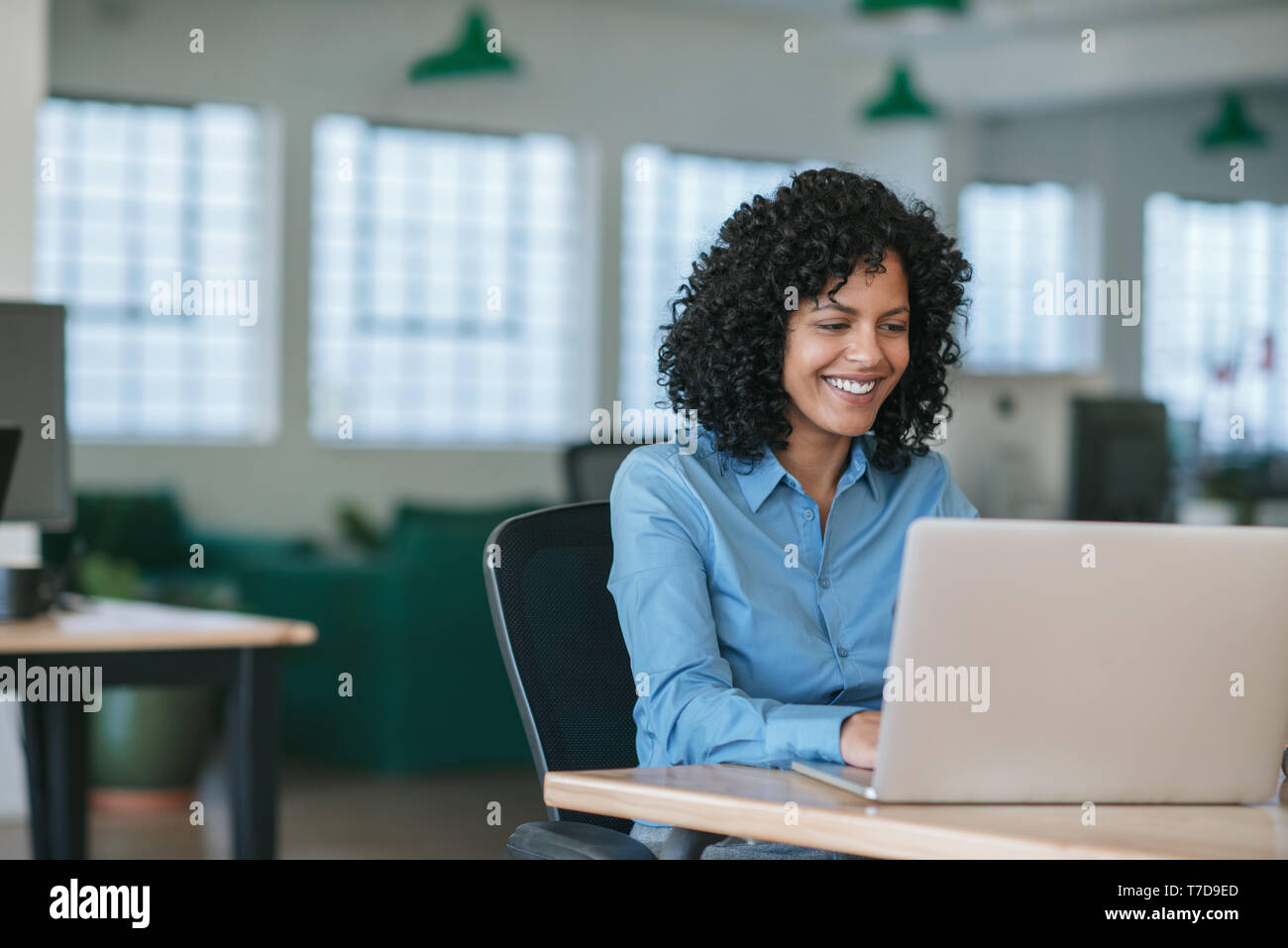 Sorridente giovane imprenditrice lavorando su un computer portatile alla sua scrivania Foto Stock