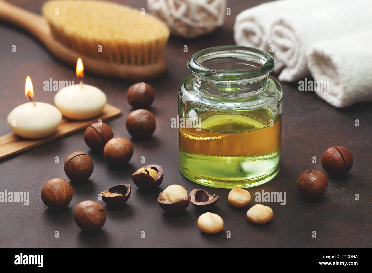 Olio di macadamia in una bottiglia di vetro, di noci di macadamia, oggetti per spa su uno sfondo marrone Foto Stock