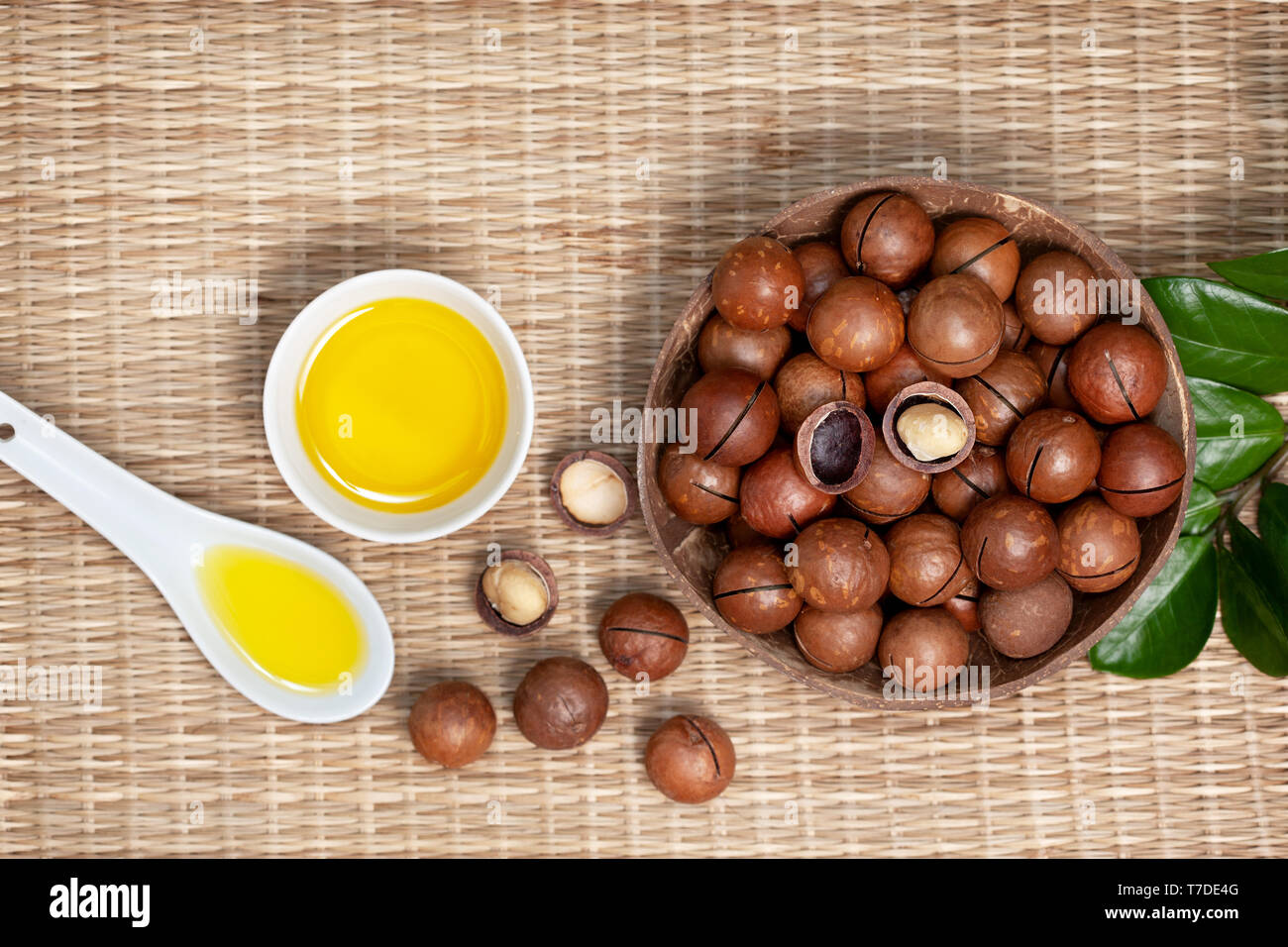 Noci di macadamia in una ciotola, olio di macadamia, olio in una vaschetta di colore bianco su una cannuccia (bambù) background. vista da sopra Foto Stock