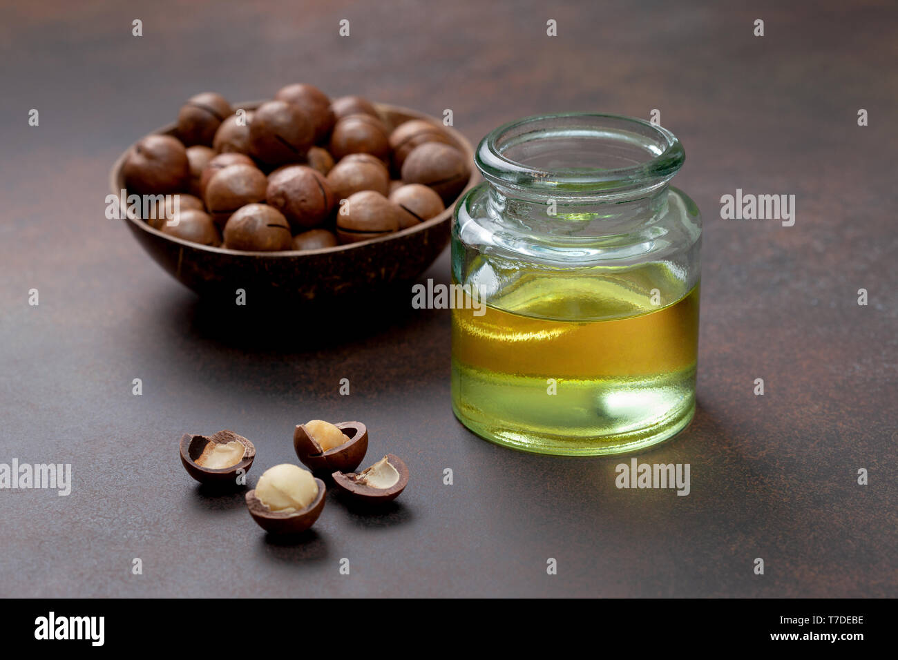 Olio di macadamia in una bottiglia di vetro, di noci di macadamia su uno sfondo marrone Foto Stock