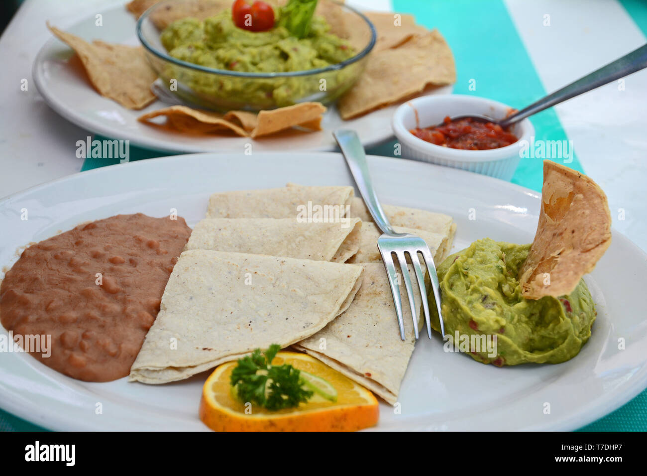 Tavolo con cibo composto da tortillas, fagioli, guacamole, salsa calda e piatti bianchi. Foto Stock