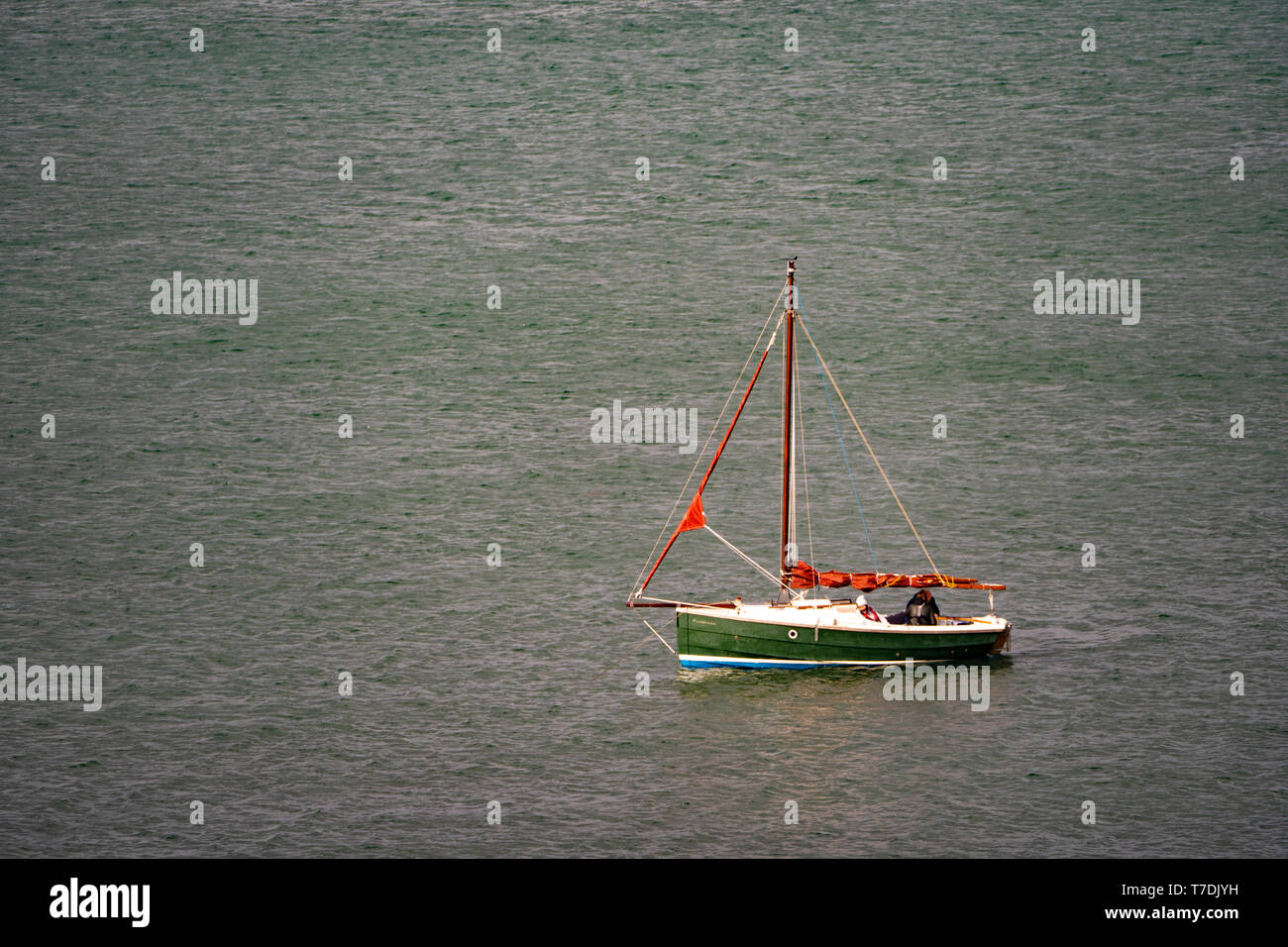 Un piccolo verde e bianco in barca a vela con un montante di rosso un no vela su un mare calmo Foto Stock