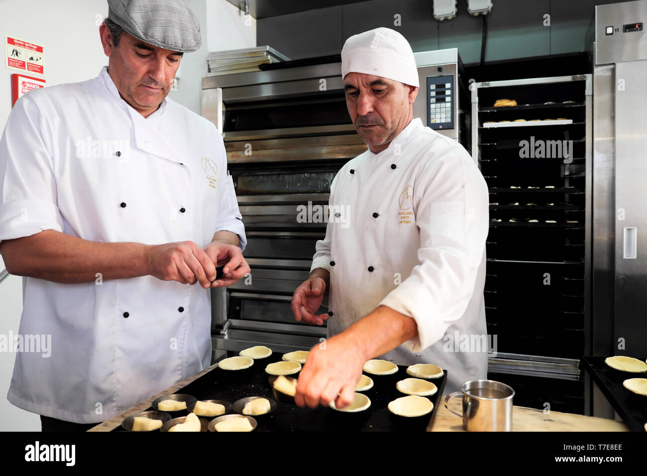 Due dipendenti di sesso maschile facendo lavoro casi di pasticceria tradizionale per Pasteis de nata crostate portoghese all'interno di una pastelaria in Alfama Lisbona KATHY DEWITT Foto Stock