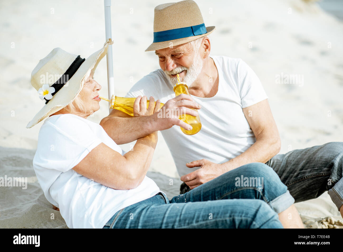 Felice coppia senior rilassante, giacente con bevande sulla spiaggia sabbiosa, godendo della loro pensione vicino al mare Foto Stock