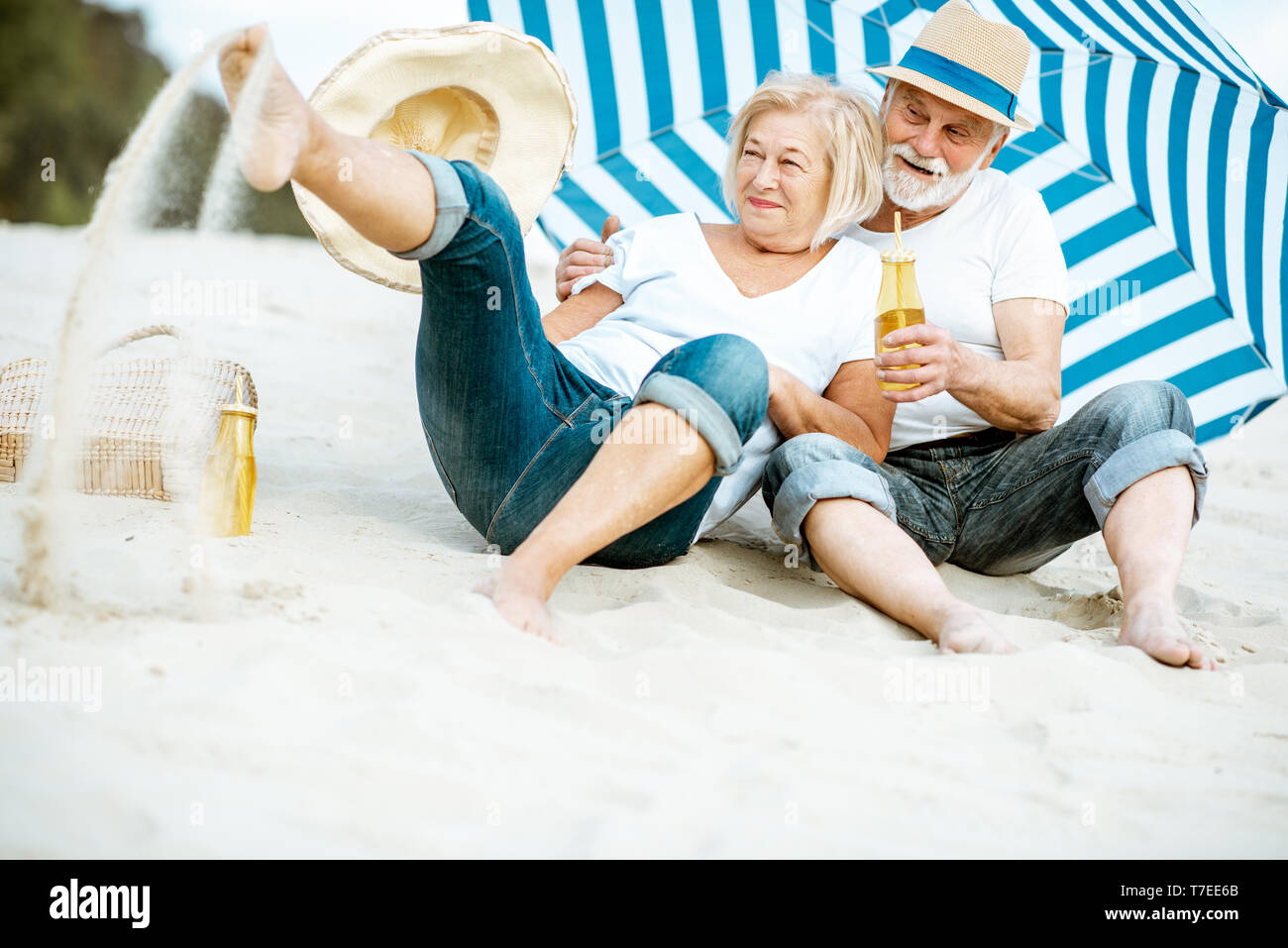 Felice coppia senior divertirsi giocando con la sabbia sulla spiaggia, godendo della loro pensione vicino al mare Foto Stock