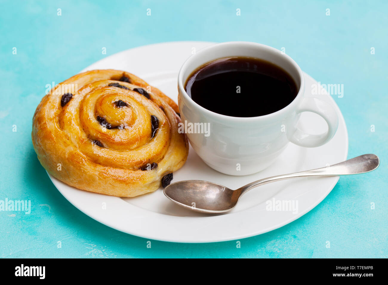 Fresca pasticceria danese con uvetta e tazza di caffè nero su sfondo blu. Close up. Foto Stock
