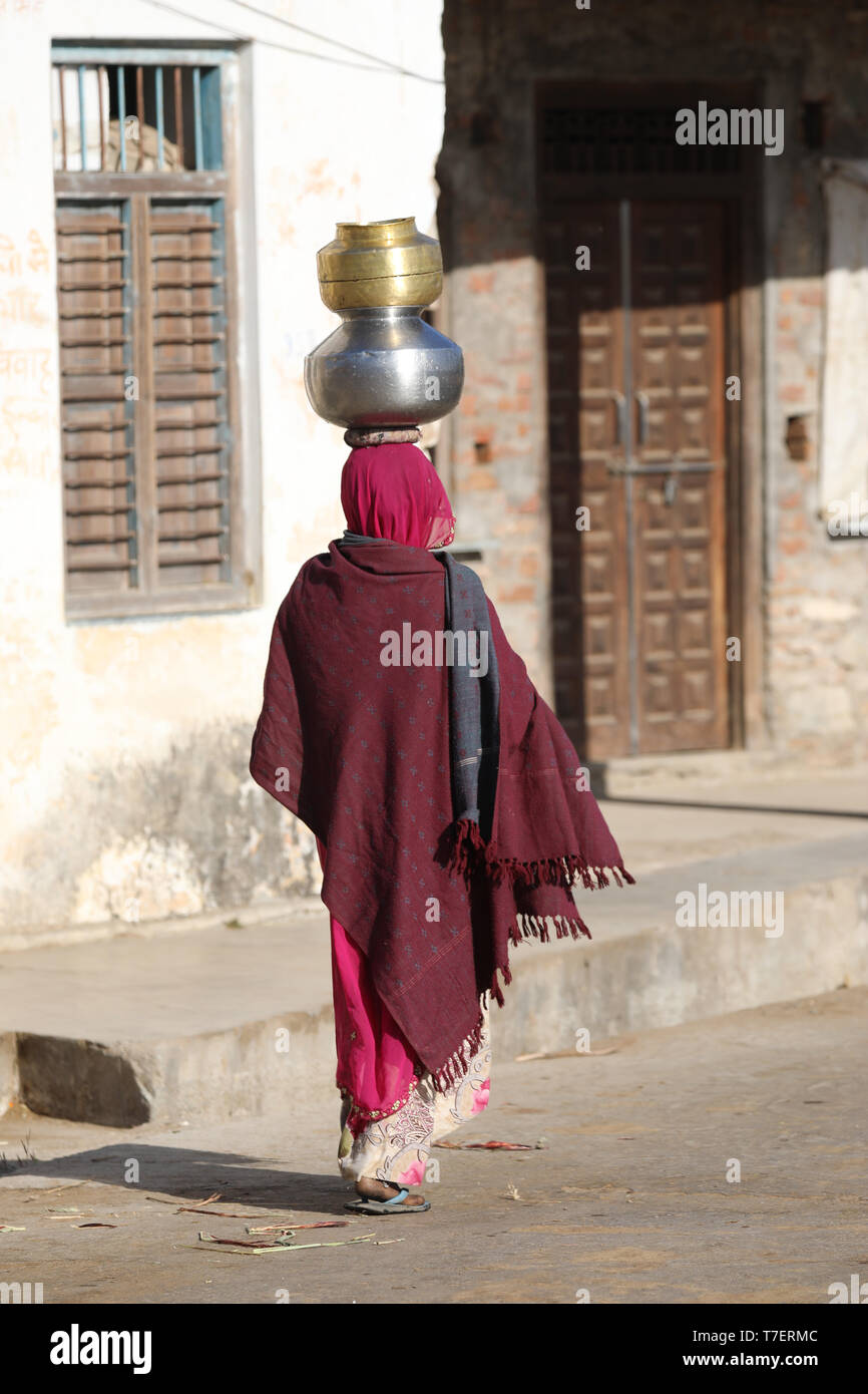 Donna portare acqua pesante ciotola sulla testa un'lungo la strada per la loro casa Foto Stock