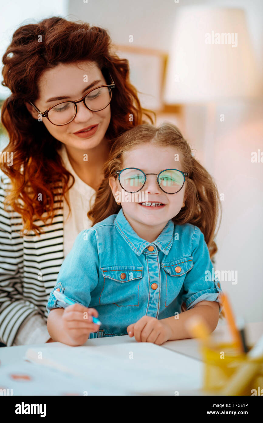 Ragazza carina con gli occhiali seduto vicino a madre lavora a casa Foto Stock