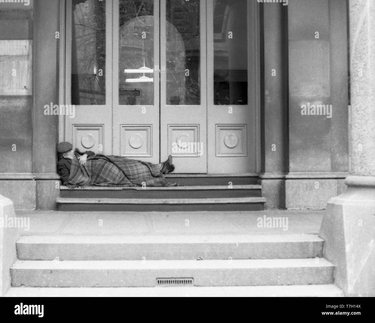 1977 Martin Place, Sydney Australia: una vecchia persona di sesso maschile, eventualmente una vagabonda o persona senzatetto dorme in uno dei portali in legno di Sydney il GPO (General Post Office). Intorno a questo tempo era comune per i senzatetto a dormire in luoghi simili lontano da pioggia e vento. Foto Stock