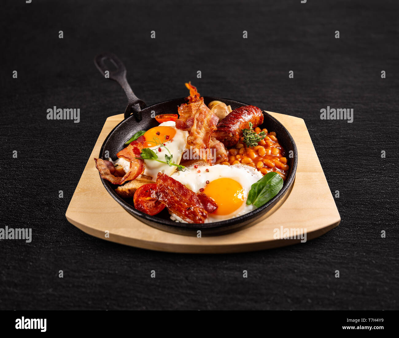 Tradizionale colazione inglese completa servita nel recipiente di cottura su sfondo nero Foto Stock
