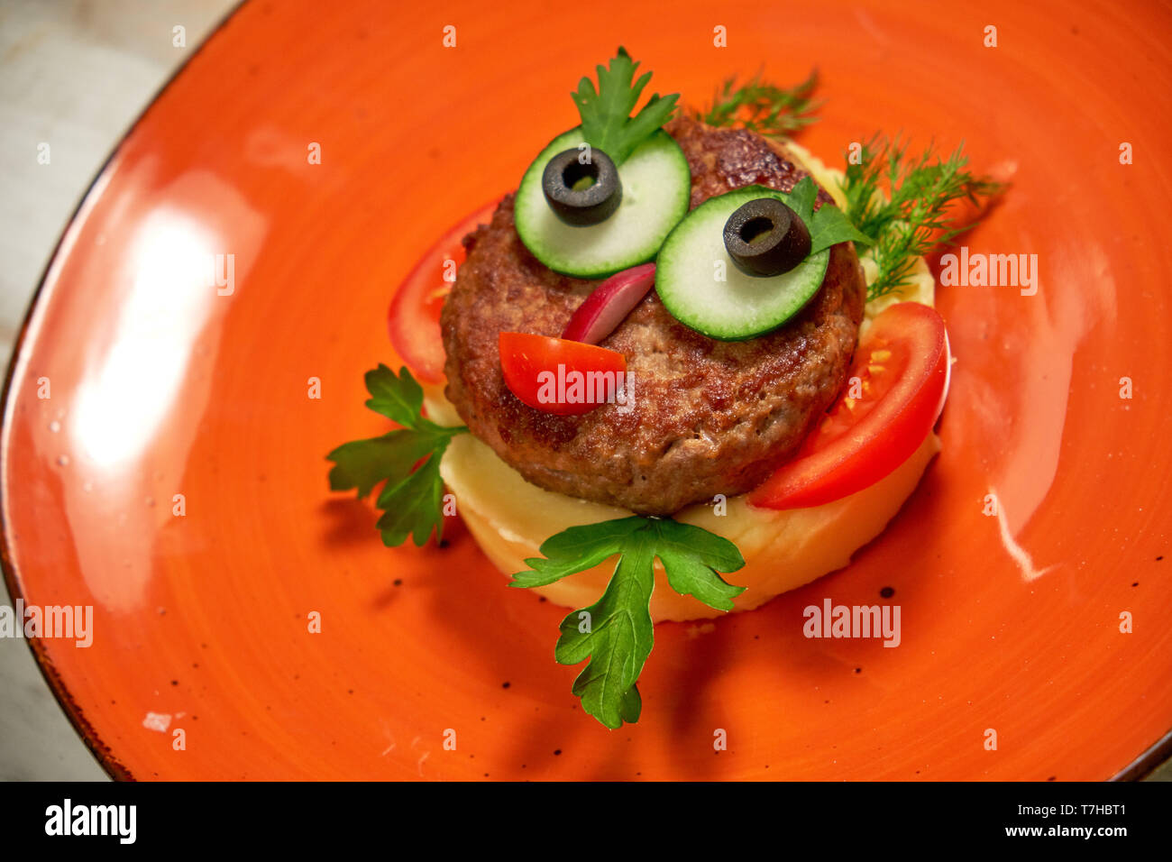 Il ristorante serve un piatto sul menu per bambini. Purea di patate con cotoletta e le verdure su una faccia arancione nella forma di una faccia Foto Stock