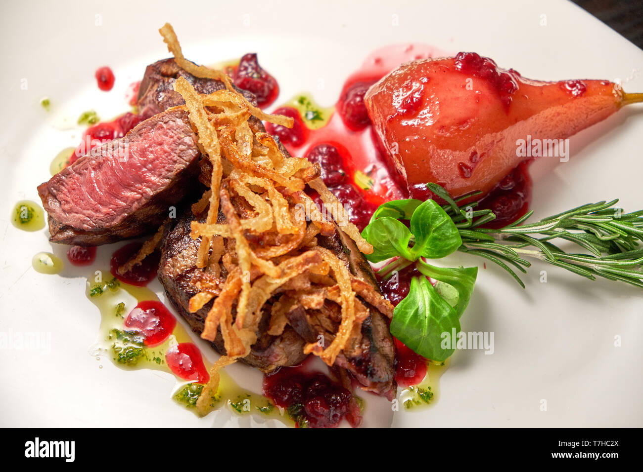 Bistecca di carne con pera su una piastra bianca decorata con verdi: rosmarino, basilico e spinaci. Legno scuro dello sfondo. Il cibo del ristorante. Foto Stock