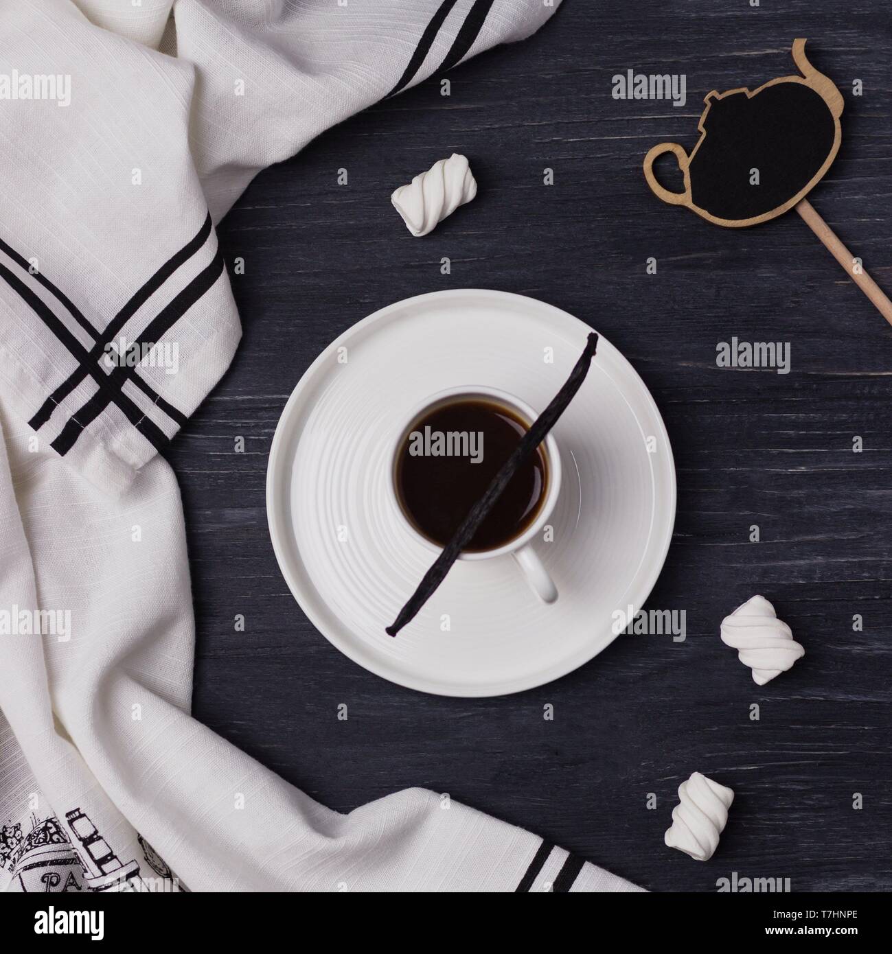 Un caffè in una tazza bianca, il baccello di vaniglia, marshmallow su un nero lo sfondo di legno. Vista superiore Foto Stock