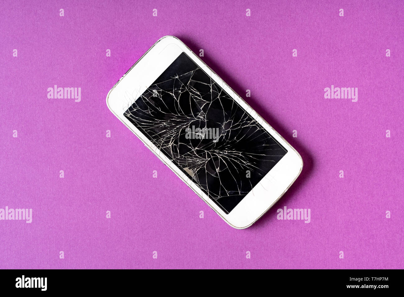 Rotto il telefono cellulare con display rotto su sfondo viola, piatto laici. Foto Stock