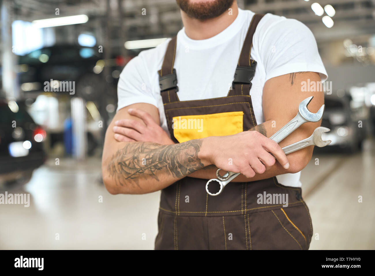 Irriconoscibile meccanica muscolare con mani tattoed, indossa in tute e white t shirt. Brutale uomo con chiavi, lavorando in autoservice. Foto Stock