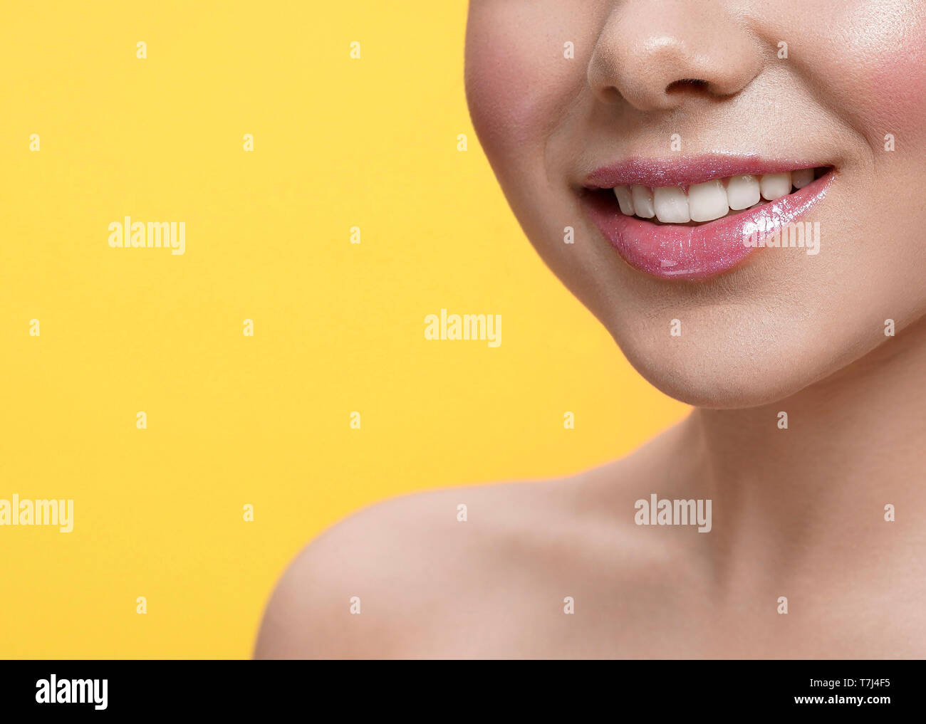 Messa a fuoco selettiva della bellissima femmina sorridere di fronte di isolato giallo dello sfondo. Modello di giovani con labbra carnose applicando lip gloss e ridere in studio. Concetto pf cosmetici e bellezza. Foto Stock