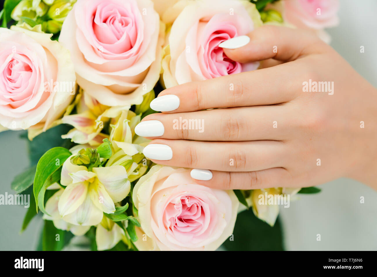 Chiodi di giovane donna con manicure bianco su un fiore rosa Foto Stock