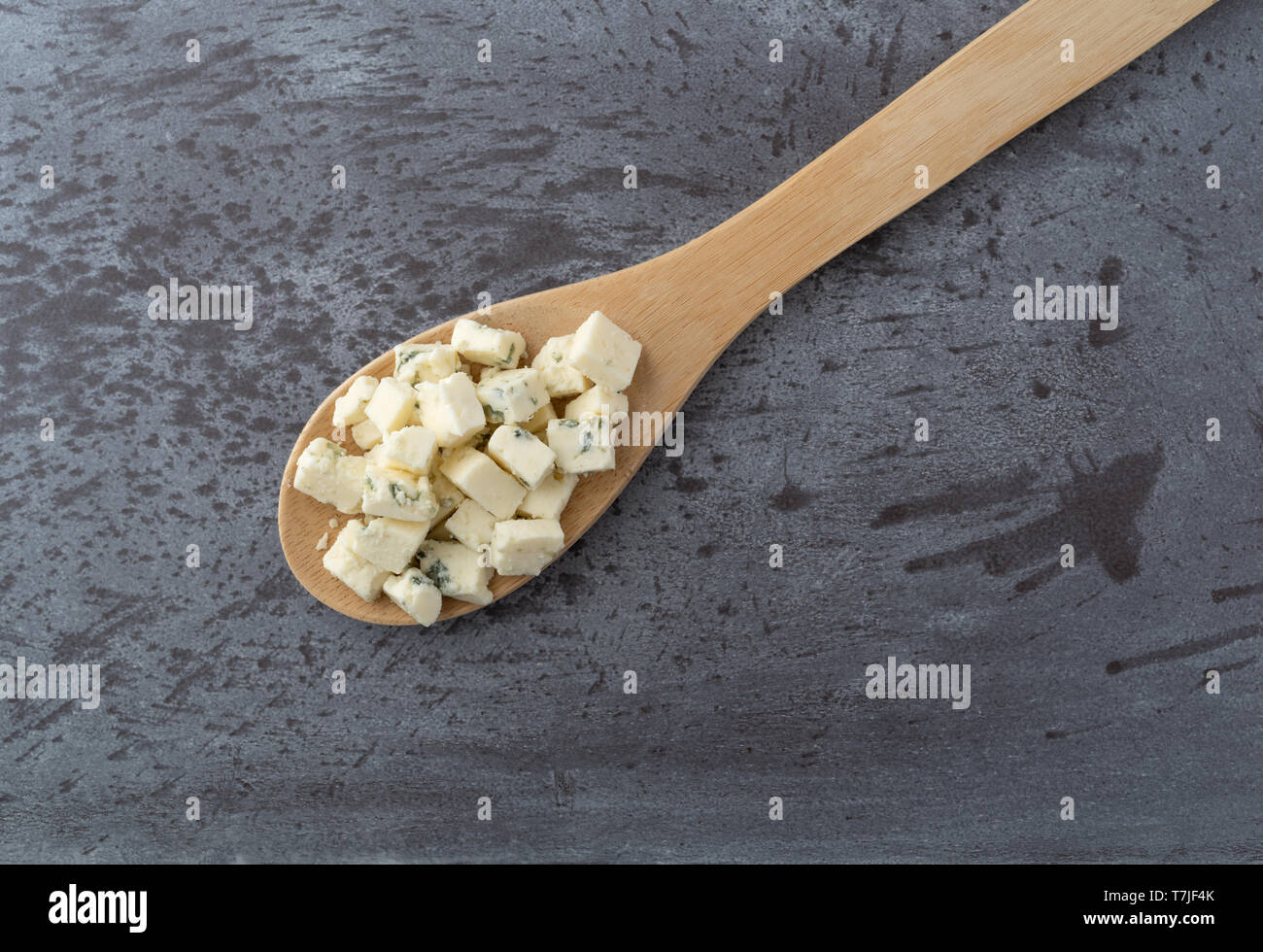 Top vista ravvicinata di una piccola porzione di sbriciolata formaggio blu su un cucchiaio di legno in cima ad uno sfondo grigio illuminato con luce naturale. Foto Stock