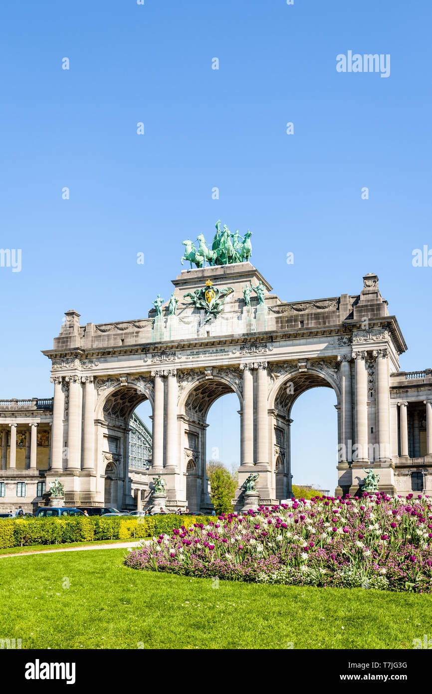 Il arcade du Cinquantenaire, l'arco trionfale nel parco del Cinquantenario a Bruxelles, in Belgio, con un aiuola di fiori in piena fioritura in primo piano. Foto Stock