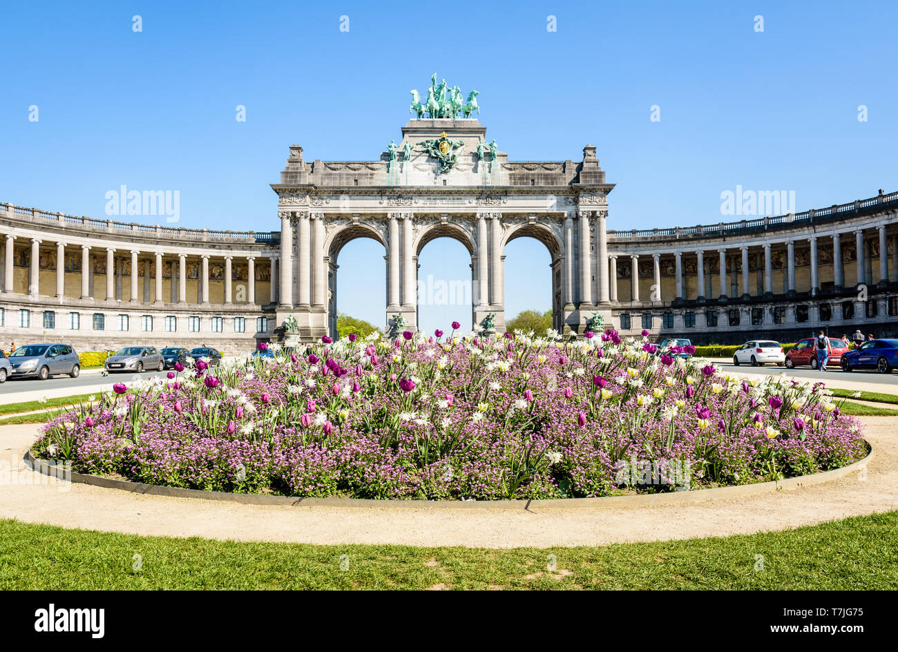 Il arcade du Cinquantenaire, l'arco trionfale nel parco del Cinquantenario a Bruxelles, in Belgio, in una giornata di sole con un aiuola di fiori in primo piano. Foto Stock