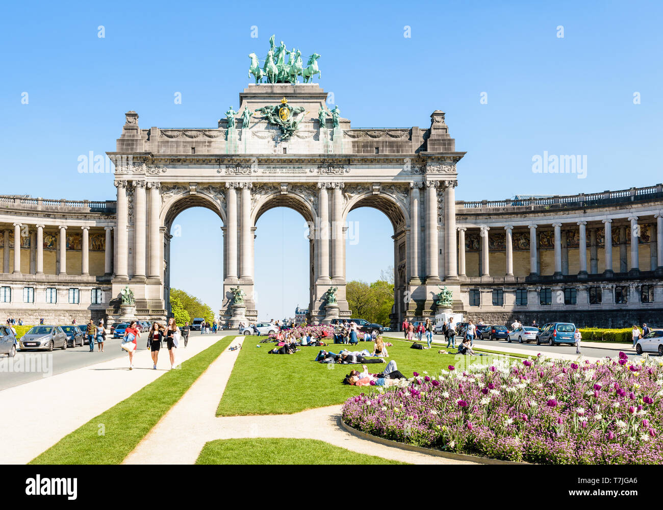Le persone godono di una giornata soleggiata ai piedi del porticato du Cinquantenaire, il monumentale arco tripla nel parco del Cinquantenario a Bruxelles, in Belgio. Foto Stock