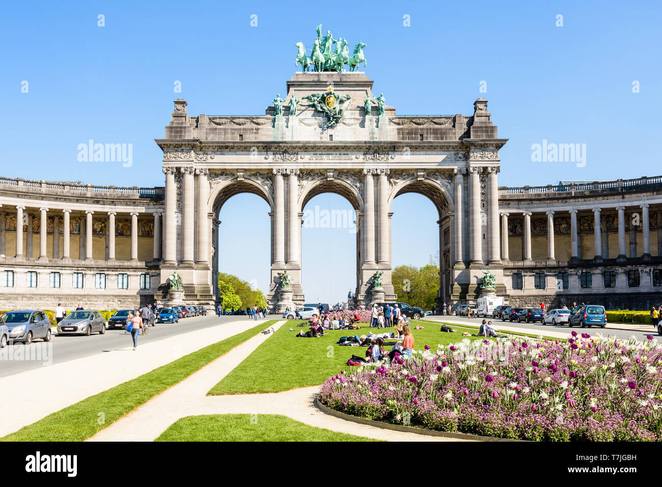 Le persone godono di una giornata soleggiata ai piedi del porticato du Cinquantenaire, il monumentale arco tripla nel parco del Cinquantenario a Bruxelles, in Belgio. Foto Stock