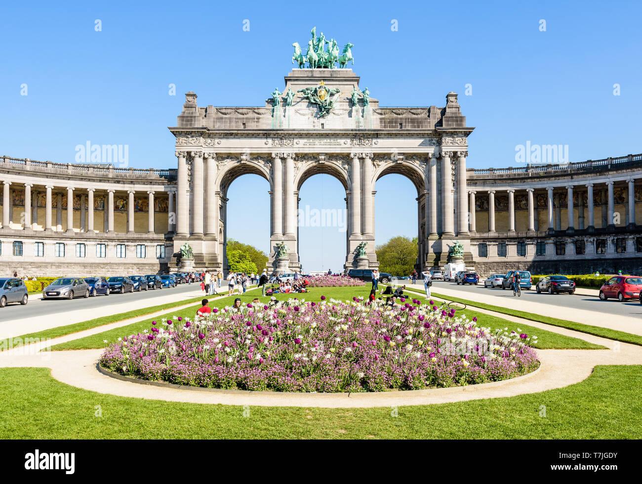 Il arcade du Cinquantenaire, l'arco trionfale nel parco del Cinquantenario a Bruxelles, in Belgio, in una giornata di sole con un aiuola di fiori in primo piano. Foto Stock