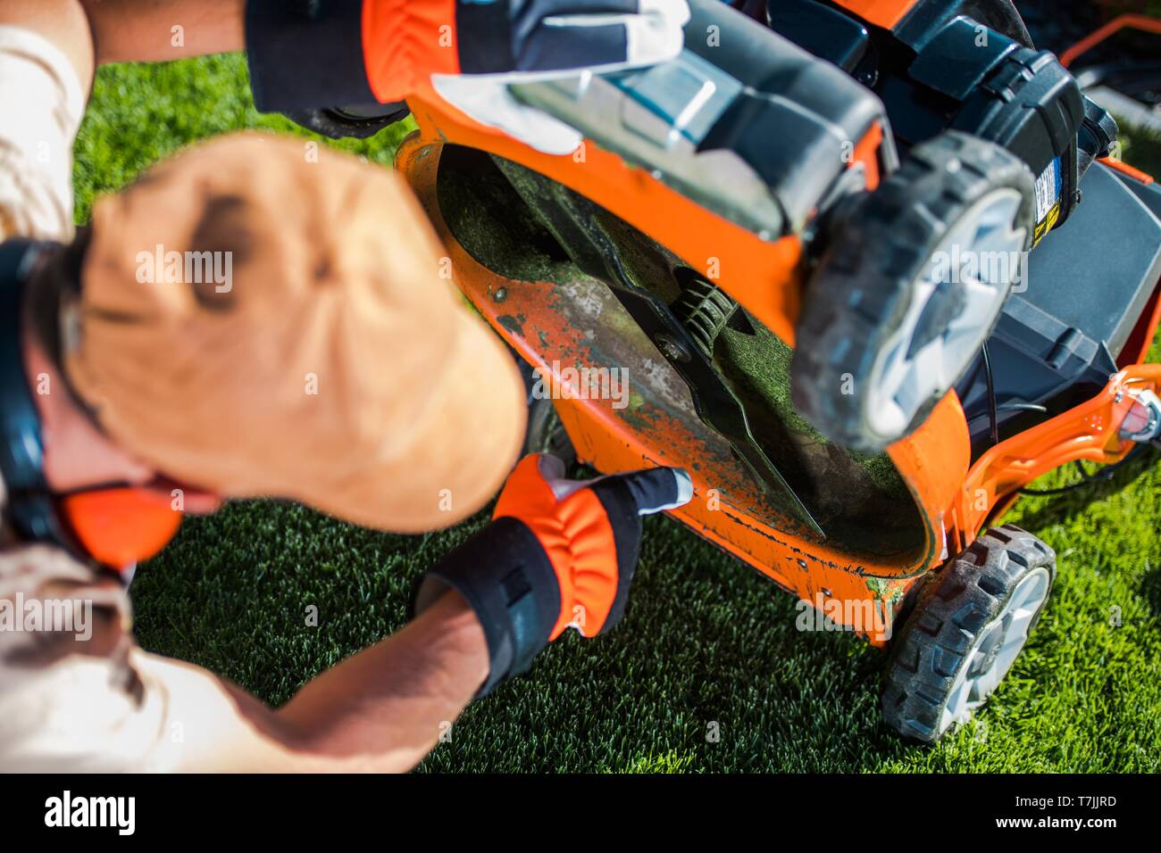 La benzina falciatrice di erba problema. Giardiniere caucasico guardando sotto la falciatrice. Paesaggistica attrezzature. Foto Stock