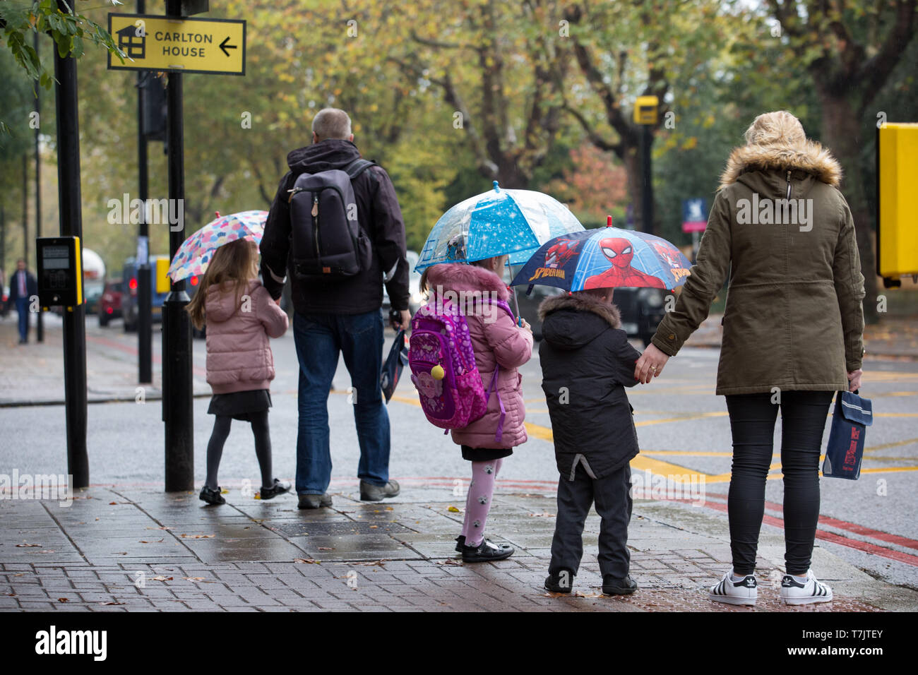 I bambini andare a scuola a piedi con i loro genitori nella pioggia ombrelli azienda in Wandsworth, Londra Foto Stock