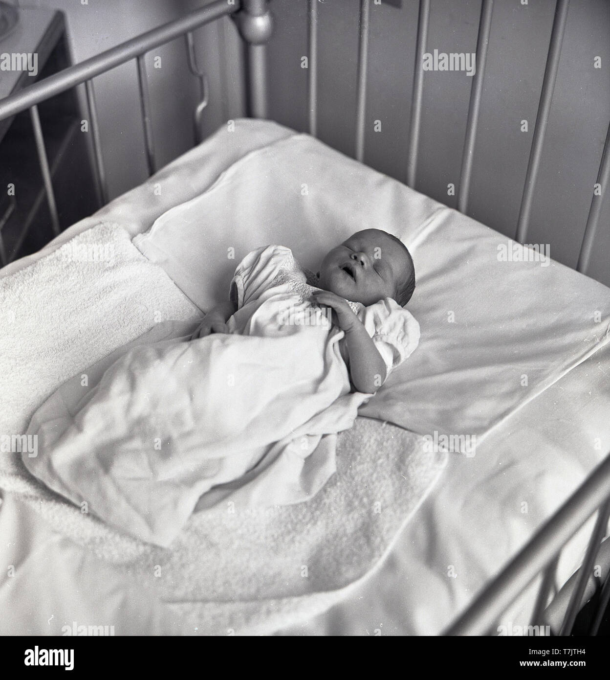 Anni sessanta, storico in un ospedale, un neonato addormentato all'interno di un metallo cot, Inghilterra, Regno Unito. Foto Stock