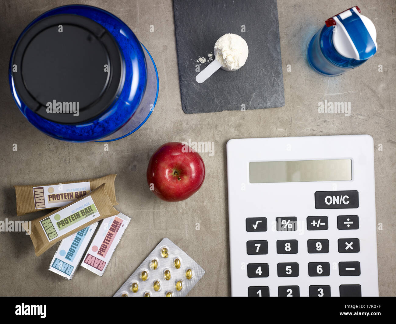 Primo piano sul big blue proteina jar, shaker, misurino con polvere, materie prime barre della proteina, rosso apple, sport supplementi in compresse e calcolatrice posa Foto Stock