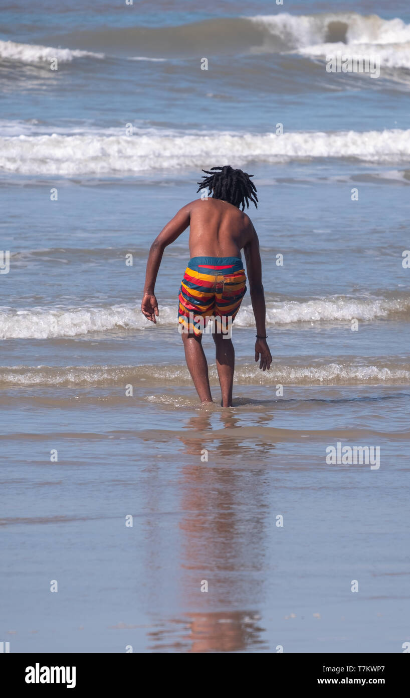 Giovane ragazzo in un colorato striped shorts riproduce le onde a Port St Johns, Transkei, Sud Africa. Il mare a Port St Johns è infestato di squali. Foto Stock