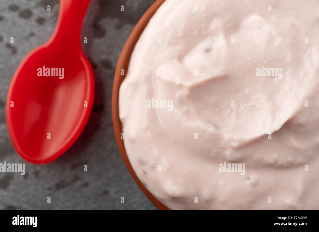 Tettuccio di chiudere la vista di una piccola ciotola di rosso lampone yogurt con un cucchiaio per lato su una tabella grigia illuminata con luce naturale. Foto Stock