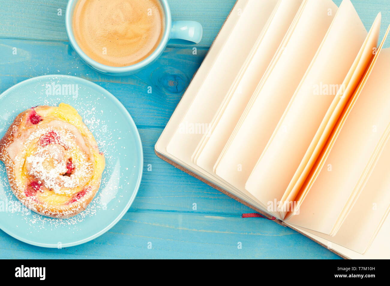 Tazza di caffè con una torta e un libro aperto su un blu sullo sfondo di legno Foto Stock