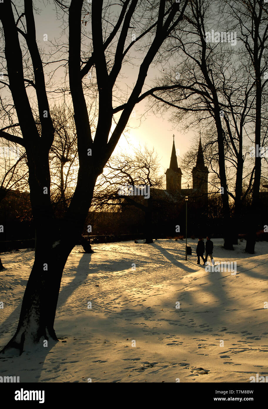 Due persone a piedi in un parco al tramonto a Tallinn in Estonia con St Charles' chiesa in background e gli alberi casting lunghe ombre sulla neve Foto Stock