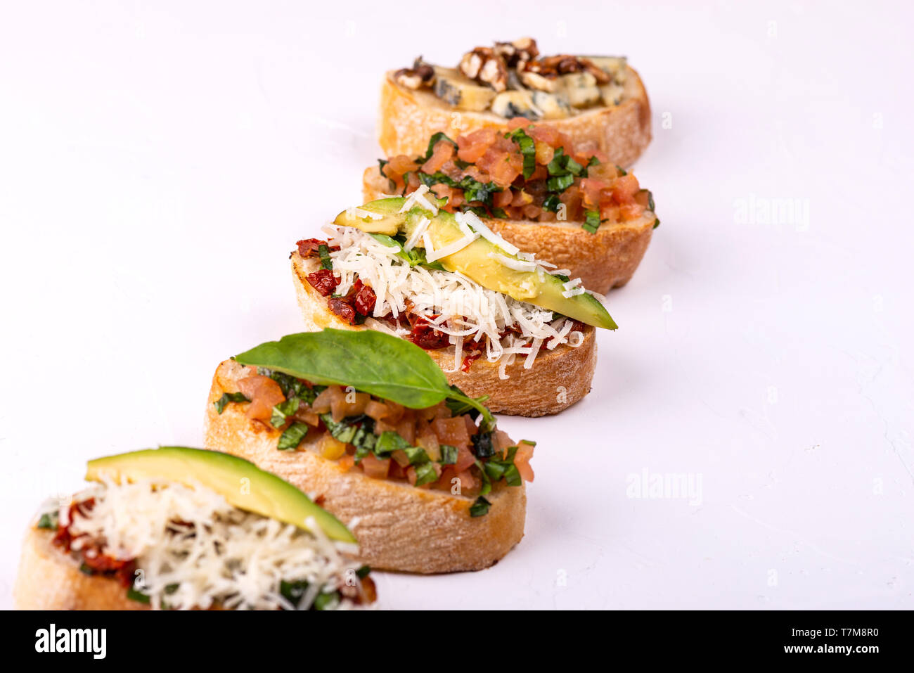 Varietà di crostino con hummus, pomodoro, avocado, formaggio, noce e verdure fresche su sfondo bianco. Vista dall'alto di snack sani concetto. Foto Stock