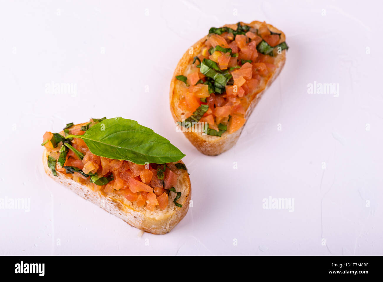Stuzzicanti pomodoro antipasti italiani o bruschetta, su fette di pane abbrustolito baguette guarnita con foglie di basilico. Foto Stock