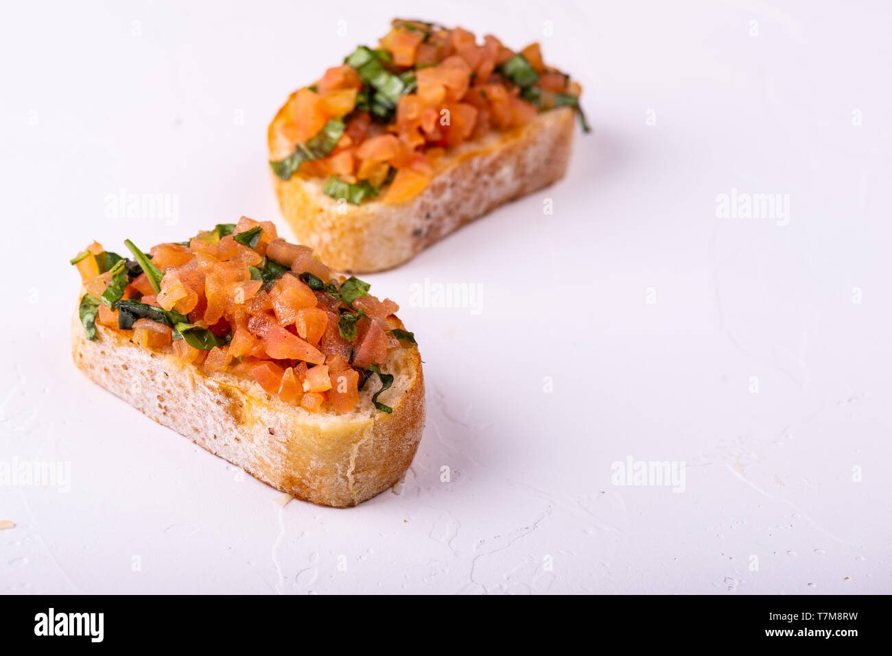 Stuzzicanti pomodoro antipasti italiani o bruschetta, su fette di pane abbrustolito baguette guarnita con foglie di basilico. Foto Stock
