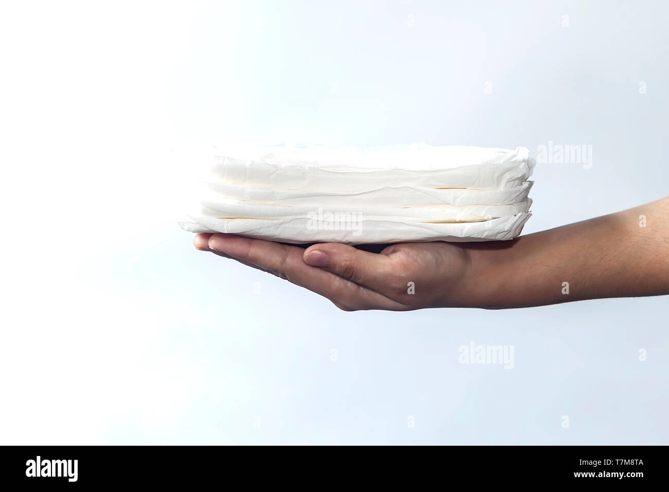 Donna di mano che tiene una pila di assorbenti igienici contro uno sfondo bianco. Periodo giorni concetto mostra femminile ciclo mestruale. Foto Stock