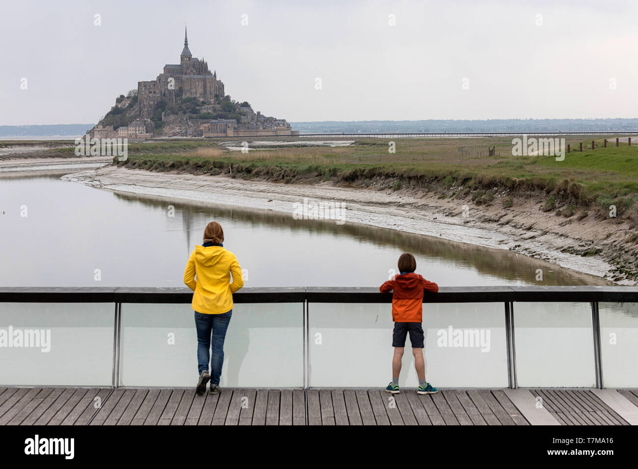 La madre e il figlio in piedi sulla passerella di legno sopra la diga sul fiume Couesnon, guardando l'isola di marea Mont Saint Michel, in Normandia, Francia Foto Stock