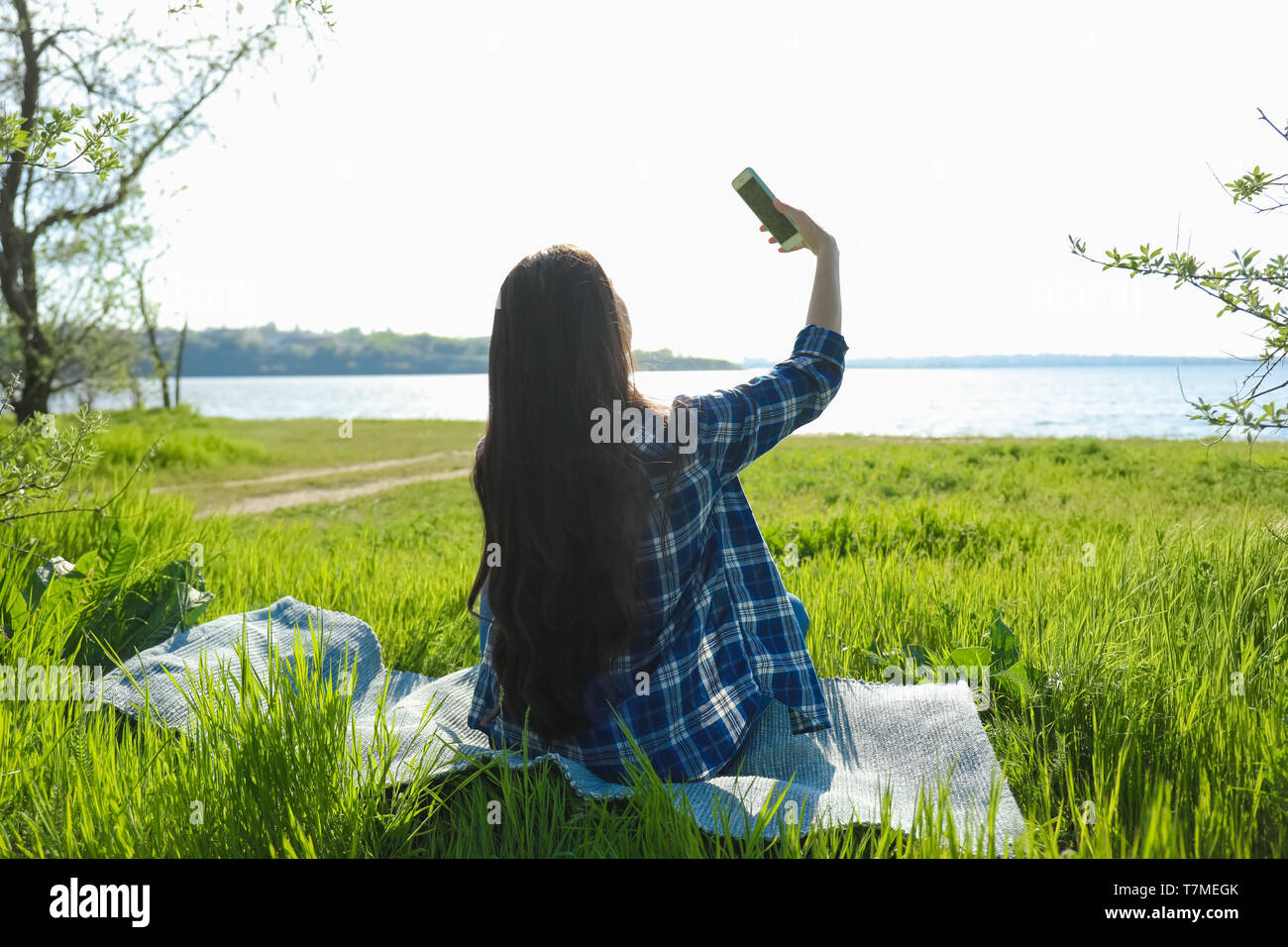 Bella giovane donna prendendo selfie vicino al fiume Foto Stock