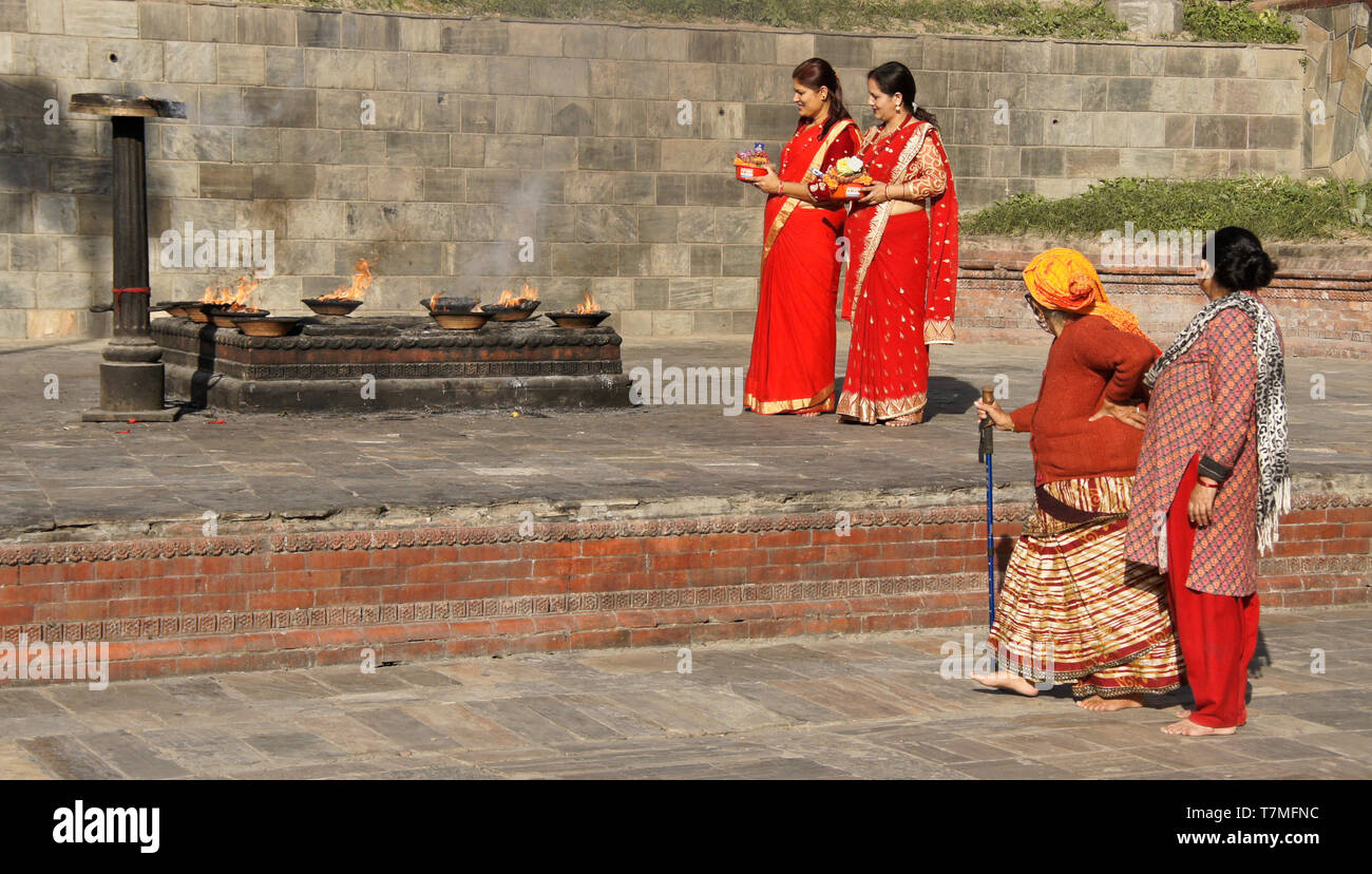 Le donne in colorate di rosso e oro con saris offerte religiosa al posto del rito del fuoco, Pashupatinath tempio indù, Valle di Kathmandu, Nepal Foto Stock