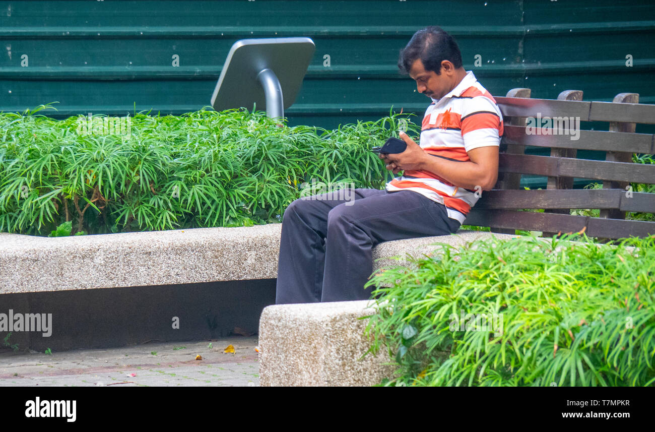 Uomo seduto su un banco di lavoro utilizzando il suo telefono mobile. Foto Stock