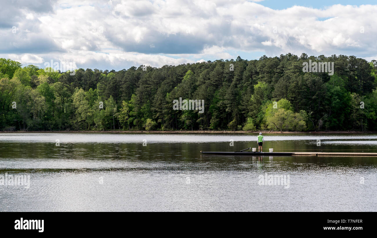 Uomo in camicia verde in piedi sul dock con due secchi e le foreste in background Foto Stock