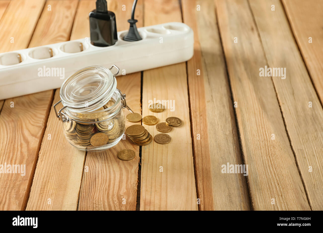 Vaso con monete e striscia di alimentazione su sfondo di legno. Risparmio di elettricità concept Foto Stock