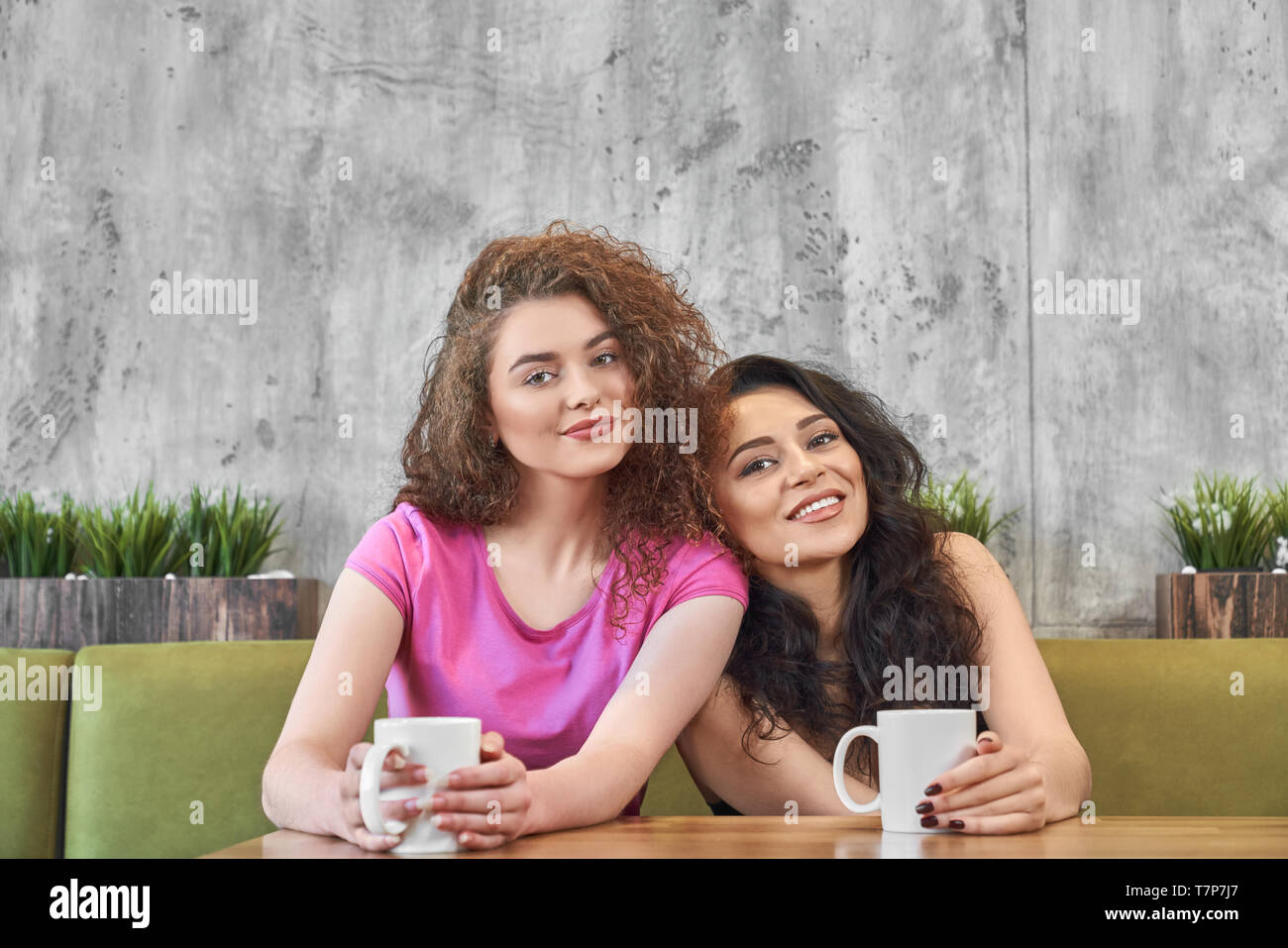 Vista frontale della bella amici di sesso femminile avente la prima  colazione nella caffetteria. Ragazze giovani seduti al tavolo e guardando  la telecamera mentre bevendo un tè caldo. Le donne di pausa