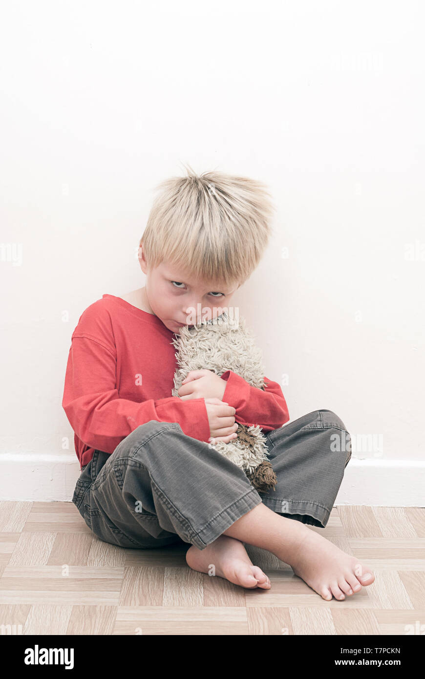 Arrabbiato sconvolto bambino seduto sul pavimento, tenendo il suo giocattolo morbido. Foto Stock
