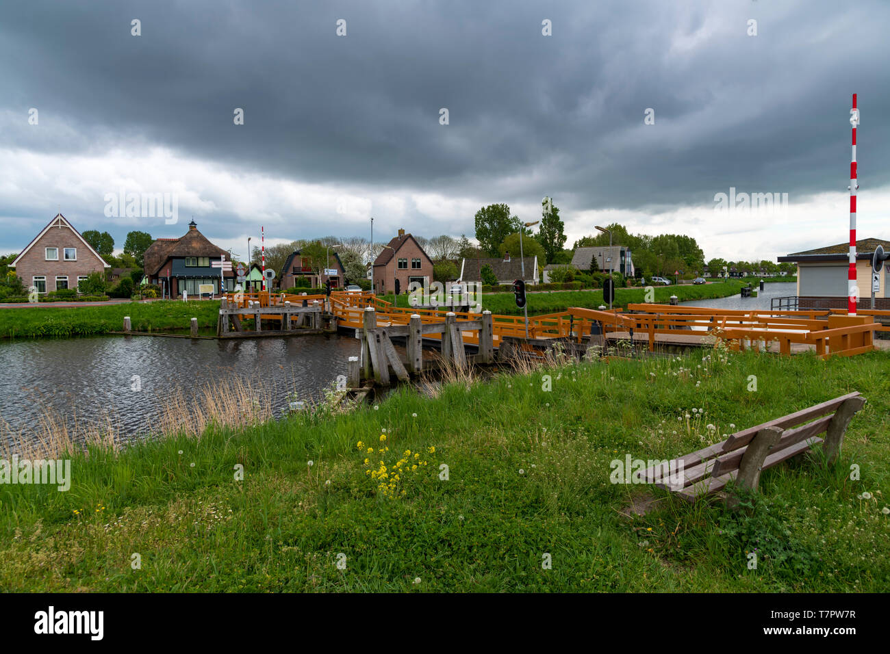 Svuotare panca di legno rivolta verso il ponte mobile sul canale sotto una pesante di raddrizzatura dark cloud e tempesta Foto Stock