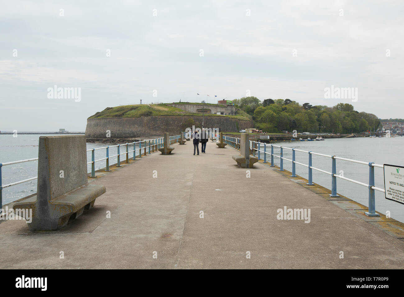 Una vista guardando shorewards del molo di pietra e la Noil Fort in background con due persone che camminano giù Pier. Weymouth Dorset England Regno Unito GB. Foto Stock