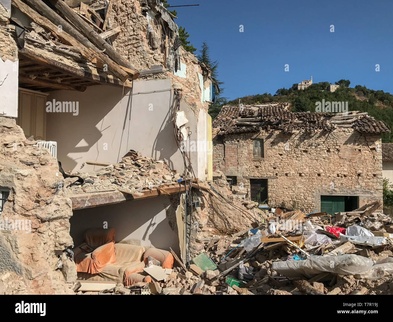 Un gravemente danneggiata casa rurale in Italia dopo un terremoto, la parete esterna è stata distrutta esponendo l'interno della casa, contro un cielo blu Foto Stock